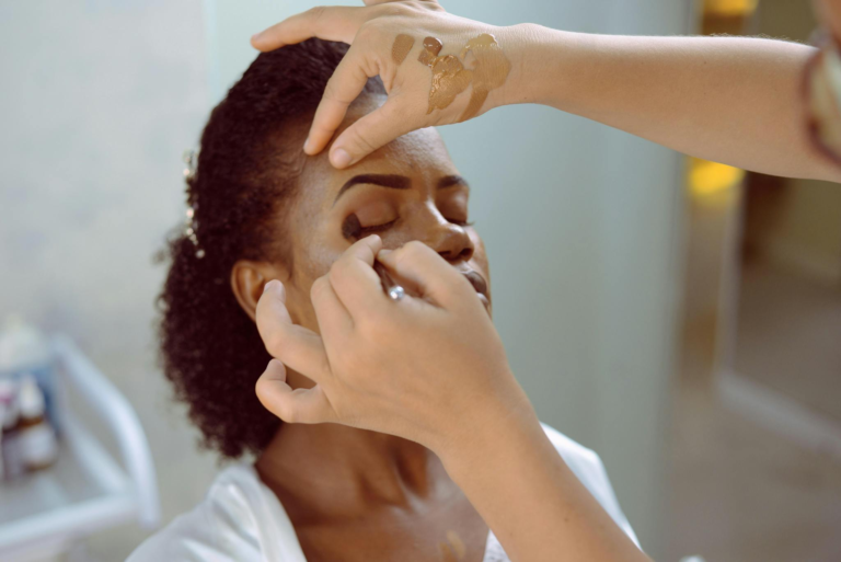 Close-up shot of a makeup artist applying eyeshadow on a black woman.